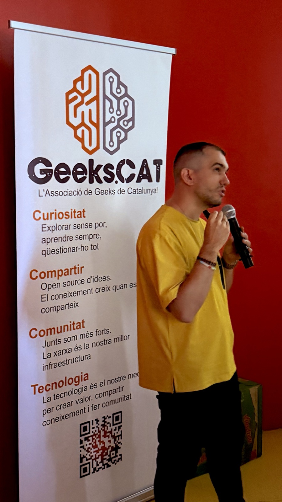 Andrey Sitnik parlant amb un micròfon al costat del cartell de GeeksCAT durant la seva xerrada