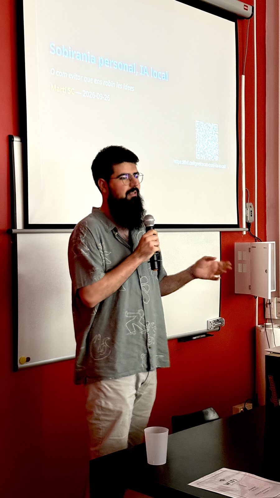 Martí Segarra parlant amb un micròfon davant de la diapositiva inicial de la seva xerrada